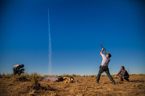 Phil Steel aims his 12 gauge shotgun at a rising model rocket while a reporter from Denver's Fox station takes video for that evening's broadcast.  
