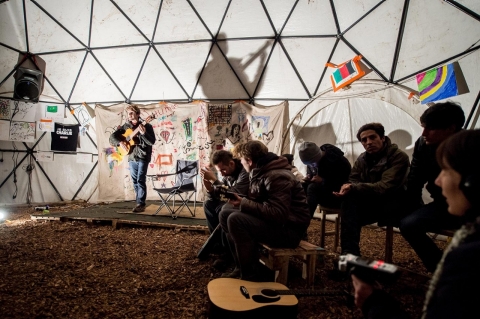 Migrants listen to a guitarist performing in a makeshift theater on Nov. 25, 2015, in the Jungle migrant camp in Calais, northern France.