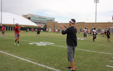 David Webb (red) tosses a football over to his head coach, Kliff Kingsbury.