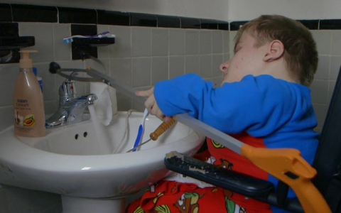 Fredrick Brennan uses a reacher arm to turn the water on in his bathroom sink.