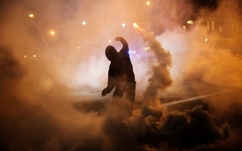 A protester throws a tear gas canister back toward riot police after a 10 p.m. curfew went into effect in Baltimore in the wake of Monday's riots following the funeral for Freddie Gray on Tuesday.