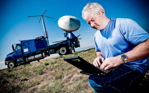 Research scientist Joshua Wurman works on his computer in the field while his Doppler on Wheels sits ready to caption data behind him.